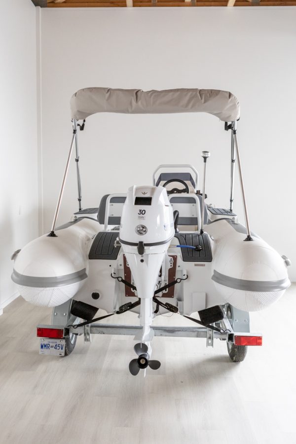 white rigid hull inflatable boat with bimini, integrated console and tohatsu outboard on road runner trailer